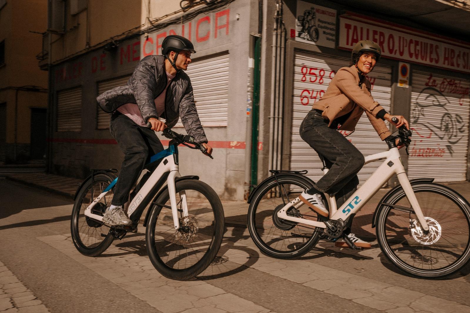 A man and a smiling woman ride modern e-bikes on a city street.