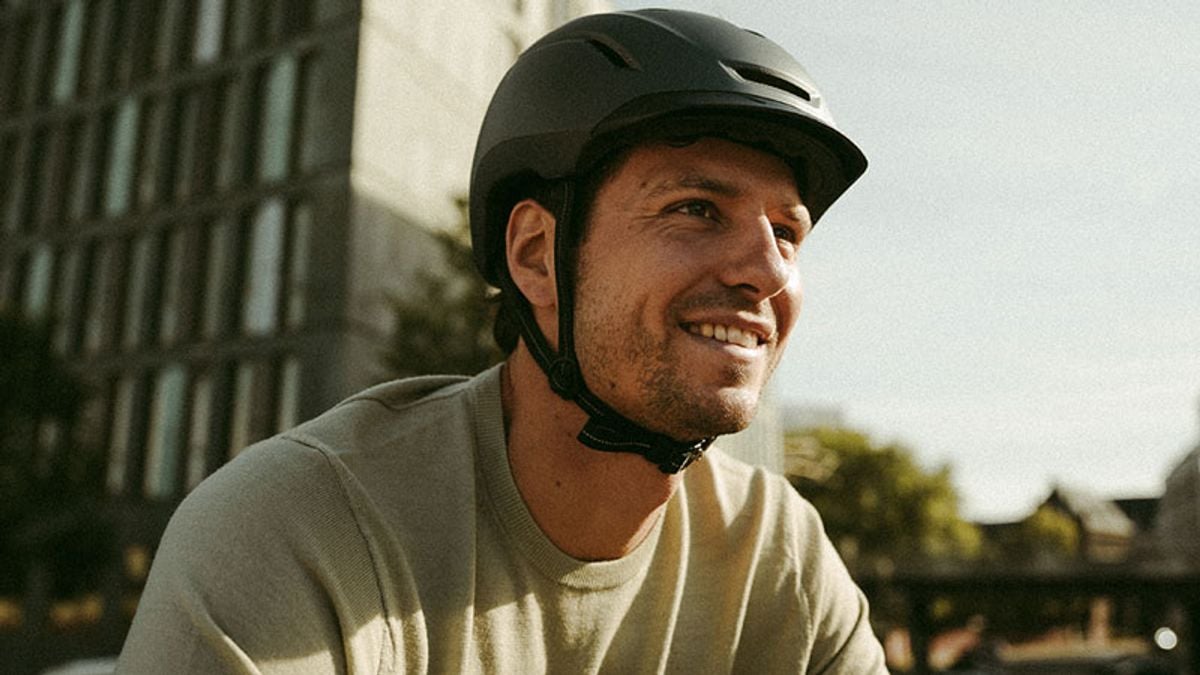 Smiling man wearing a dark grey helmet outdoors.