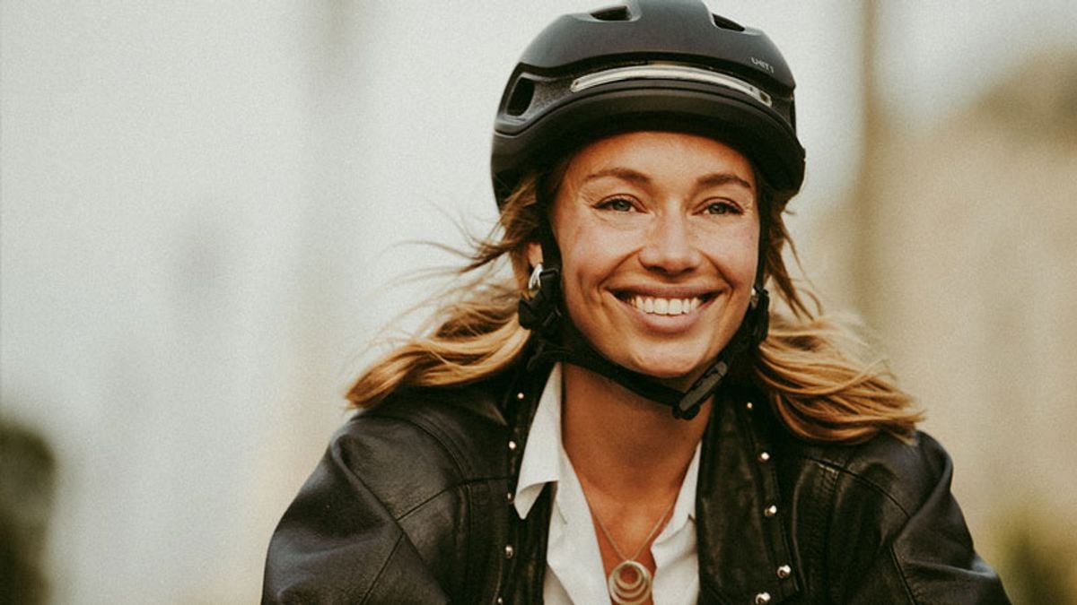 A smiling woman with blonde hair wears a black helmet and leather jacket.