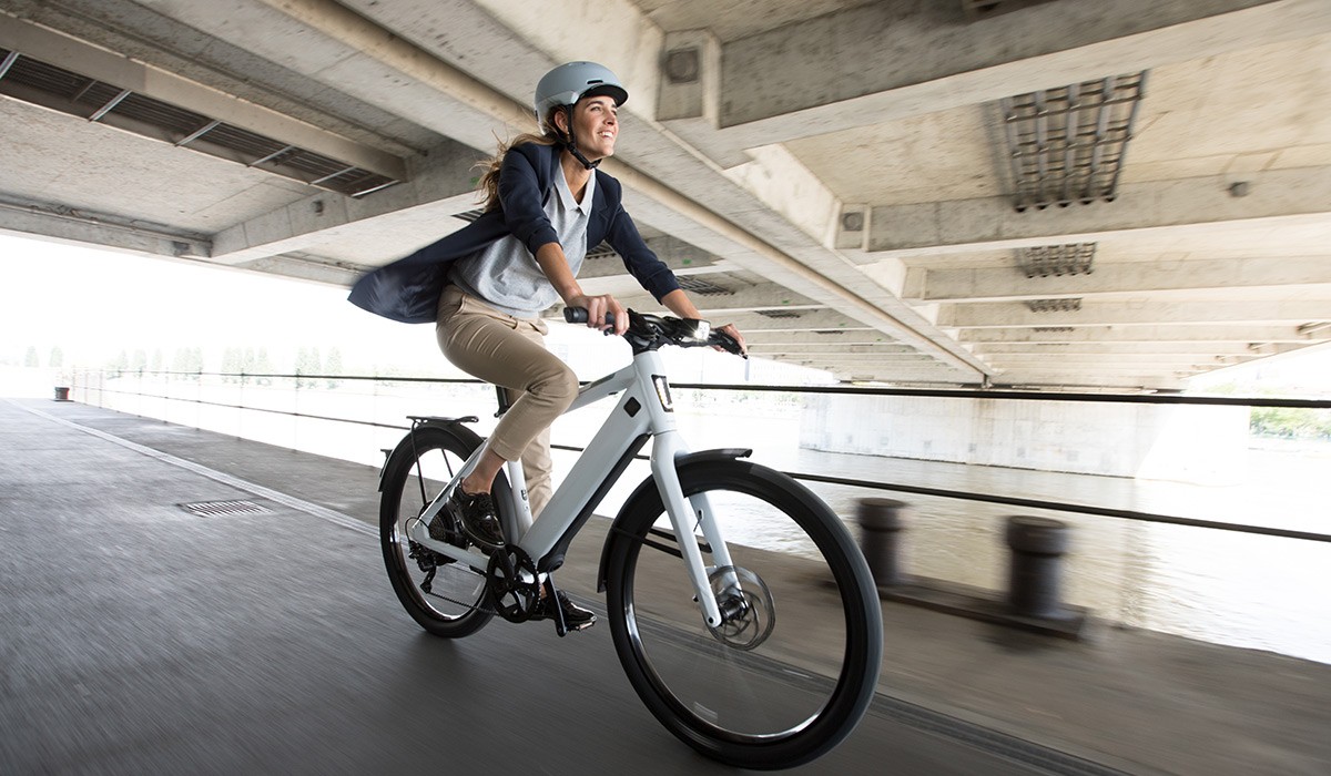 Déplacements sereins et sûrs avec une assurance vélo électrique : une femme roule le long d'une rivière avec son vélo électrique Stromer.
